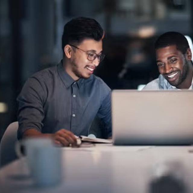 Two men talking over a laptop representing the importance of collaboration. 