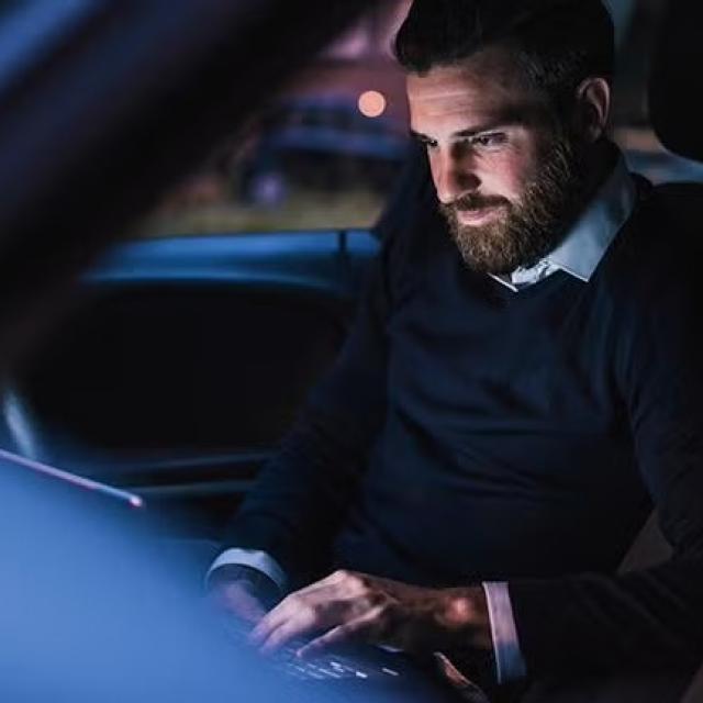 Man working on a laptop while sitting in a car demonstrating the importance of duty of care for travelling employees.