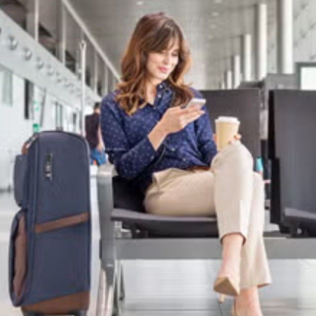 A woman sitting in the airport next to her suitcase representing the importance of sustainability in business travel. 