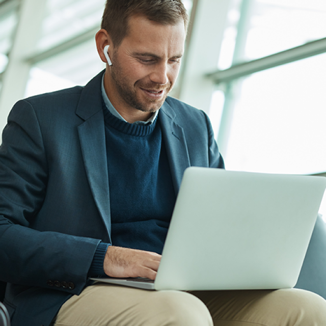 Man working on a laptop while seated in an airport representing how Corporate Traveller delivers technology and expense solutions that allow you to manage your travel, get vital information about your travel patterns and stay in control of your travel expenses.